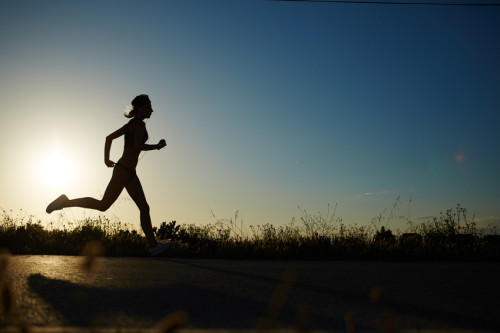 Silhouette of athletic girl running down the road to a sunset